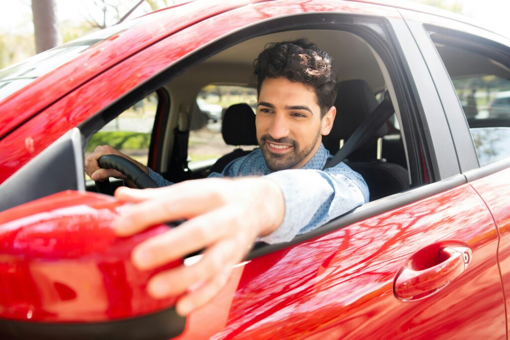 Man moving rear view wing mirror in car.